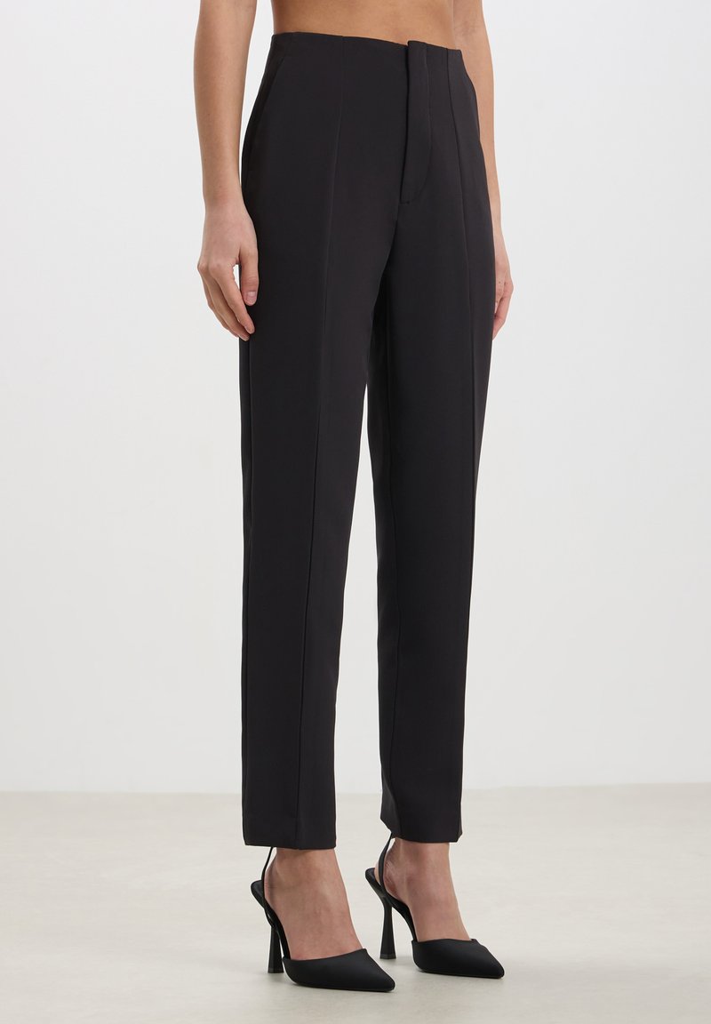 Pantalons noirs taille haute en tissu lisse et structuré. Dotés d'une fermeture éclair à l'avant et de jambes droites avec une coupe ajustée.