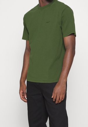 Koszulka z krótkim rękawem i okrągłym dekoltem w kolorze ciemnej zieleni, wykonana z bawełny, z subtelnym logo Levi's na piersi. W zestawie z czarnymi spodniami.