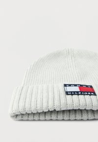 Lysegrå strikket lue med et brettet ribbestrikket design, med en flerfarget Tommy Hilfiger-logo på siden.