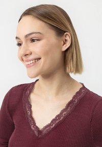 Top côtelé bordeaux avec un décolleté en V agrémenté de dentelle. Texture douce, coupe ajustée et manches courtes. Design minimaliste sur fond clair.