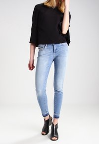 Svart kort topp med utsvängda ärmar, ljusblå skinny jeans och svarta öppna klackskor med blixtlås och utskärningar.