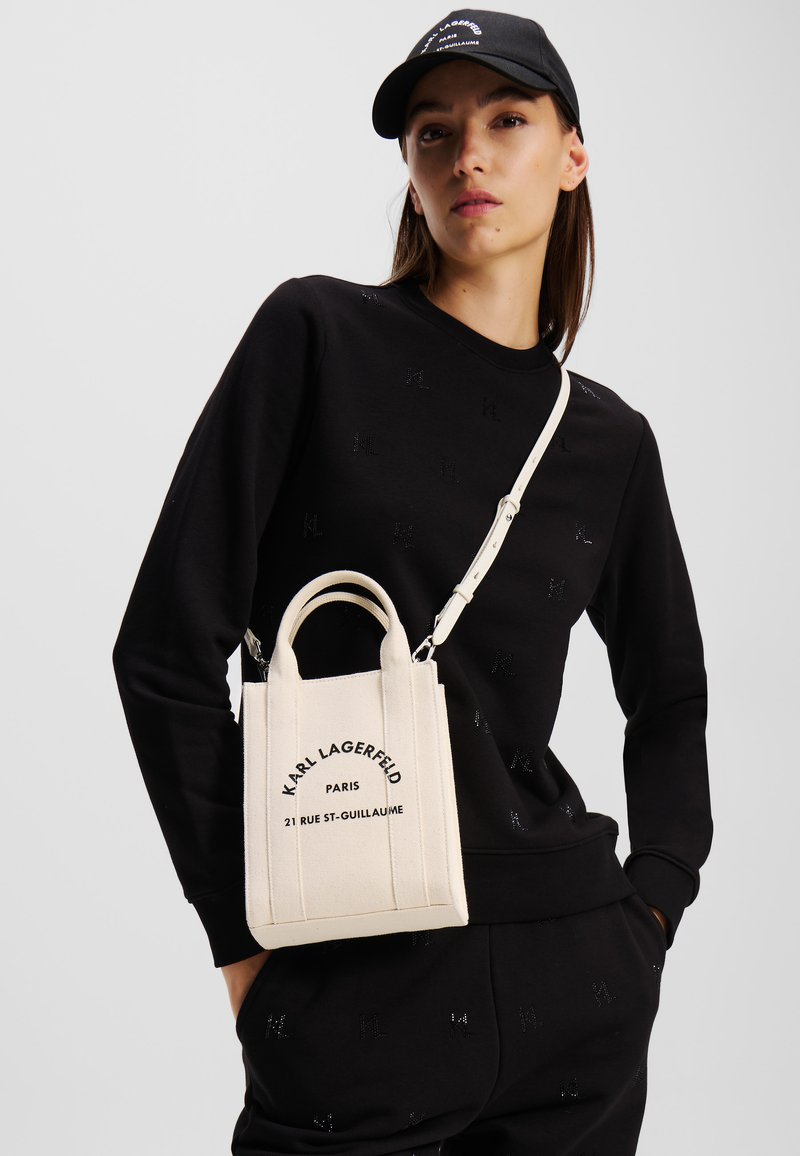Borsa in tela avorio con doppi manici superiori e tracolla staccabile, con testo nero: "KARL LAGERFELD PARIS 21 RUE ST-GUILLAUME."