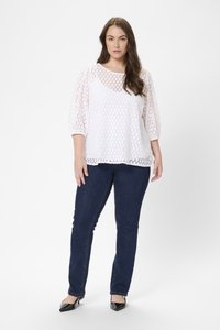 Vit spetsblus med trekvartslånga ärmar, mönstrad med utskurna cirklar; kombinerad med mörkblå slim-fit jeans och svarta spetsiga klackskor.