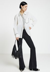 White button-up shirt with black piping, black flared jeans, and a fringed black handbag. Silver accents on shoes. Smooth texture throughout.