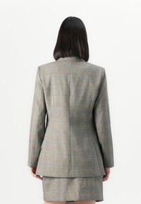 Grå rutete blazer med en strukturert design, som har en enkel bakre splitt og en skreddersydd passform, kombinert med et matchende rutet skjørt.