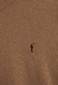 Brun stickad tröja med en strukturerad yta, med en liten marinblå logotyp av en gående figur på vänster sida.