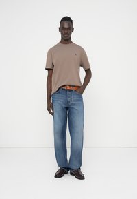 Καφέ κοντομάνικο μπλουζάκι με μικρό λογότυπο, συνδυασμένο με μπλε τζιν με ίσια γραμμή και καφέ ζώνη, ολοκληρωμένο με μαύρα παπούτσια.