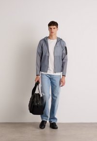 Gray lightweight jacket with hood, front zipper, and side pockets. Worn over a white t-shirt and light blue jeans. Black shoes and bag.