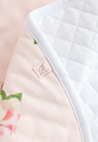 Floral-patterned blanket featuring a soft pink fabric on one side and a quilted white fabric on the other, edged with white trim.