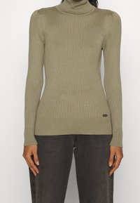 Sweter z golfem w oliwkowym kolorze, dopasowany krój, długie rękawy, z subtelnymi detali w postaci bufiastych ramion oraz metką z logo na dole.
