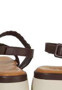 Sandales en cuir marron avec des brides tressées sur l'avant du pied, une petite bride de cheville et une semelle de plate-forme blanche. Semelle intérieure texturée pour le confort.
