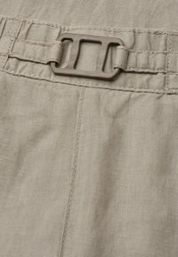 Tissu beige avec une couture cousue et une boucle rectangulaire en plastique fixée à une sangle réglable.