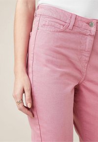 Pantalons en denim rose clair avec une texture légèrement délavée, dotés d'une conception à cinq poches et d'une fermeture à bouton métallique à la taille.