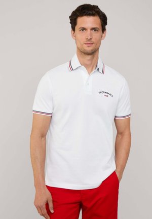 Weißes Poloshirt mit rot-blau gestreiftem Kragen und Ärmeln, mit einem kleinen gestickten Logo auf der Brust. Kurze Ärmel.