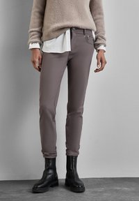 Bruine zachte stofbroek met een slim fit, voorzien van een rits en knoopsluiting, en voorzakken, gecombineerd met een beige harige trui en zwarte laarzen.