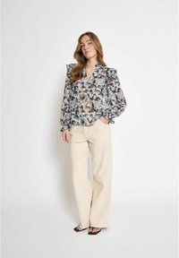 Blouse transparente dans un motif abstrait bleu clair et gris, avec un col en V, des manches volantes et une coupe ample, associée à un pantalon large beige.