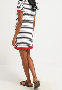 Robe rayée à manches courtes, avec une bordure en dentelle rouge à l'ourlet, fabriquée en tissu doux. Portée avec des sandales noires, affichant une coupe décontractée et un style casual.