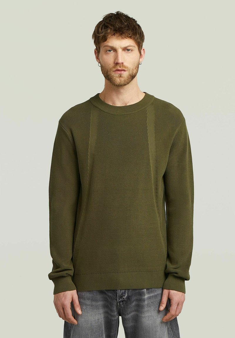 Pull en tricot vert olive avec une texture côtelée, encolure ronde et manches longues. Présente des détails de couture verticaux sur le devant.