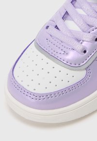 Sapatilhas de couro sintético roxo com caixa de bico perfurada branca, detalhes lisos em lavanda e cordões metálicos roxos. Sola redonda branca.