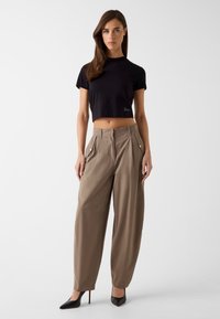 Zwart crop top met korte mouwen met logodetail, gecombineerd met beige, taillehoge broek met plooien en goudkleurige knopen. Zwarte hakken.