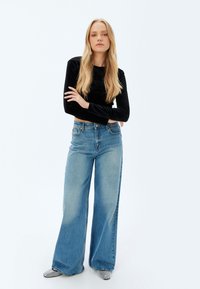 Maglietta nera a maniche lunghe abbinata a jeans a gamba larga blu chiaro e scarpe argentate texturizzate. Design semplice con linee pulite e dettagli minimi.