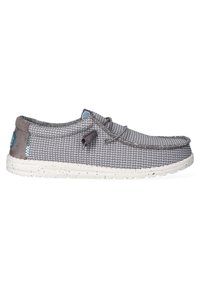 Zapato textil gris con textura tejida, cuello gris acolchado y suela salpicada de blanco. Presenta un logo azul y detalle de cordones ajustables.