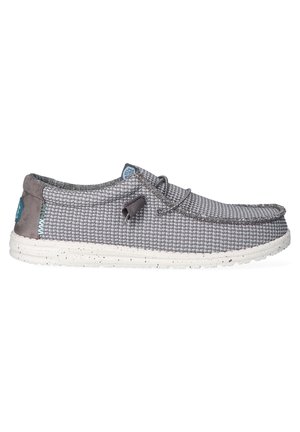 Zapato textil gris con textura tejida, cuello gris acolchado y suela salpicada de blanco. Presenta un logo azul y detalle de cordones ajustables.