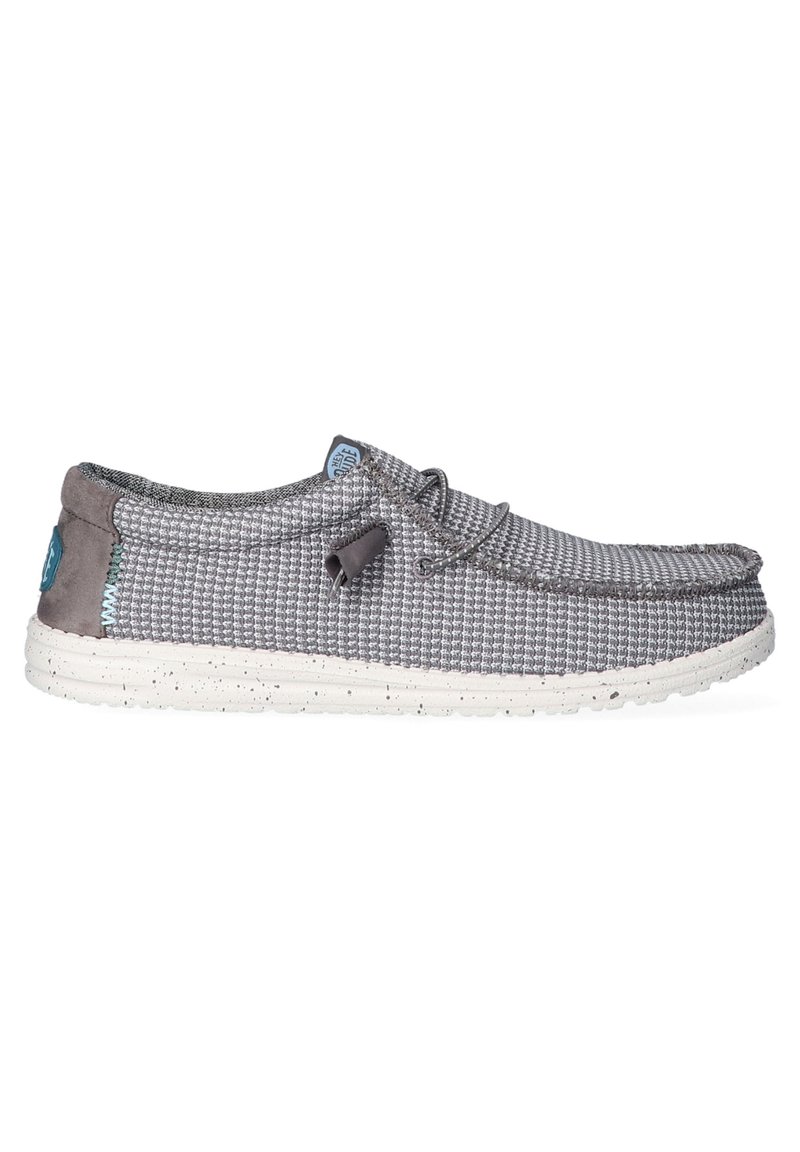 Zapato textil gris con textura tejida, cuello gris acolchado y suela salpicada de blanco. Presenta un logo azul y detalle de cordones ajustables.