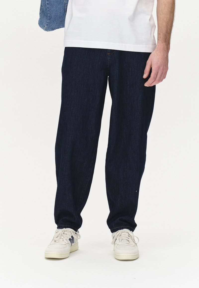 Temno modri jeans hlače ohlapnega kroja, z teksturirano površino in rumenim šivom. V kombinaciji z belimi supergami.