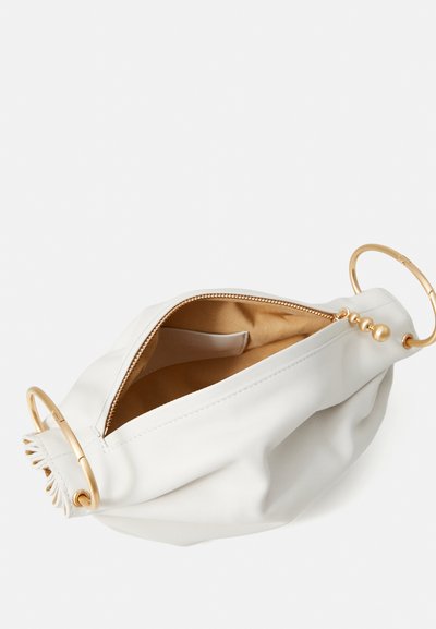 Balta ādas soma ar zelta riņķa akcentiem un aizveramu augšu. Mīksta, teksturēta ārpuse ar gludu bēšas krāsas iekšpusi. Redzama iekšējā etiķete.