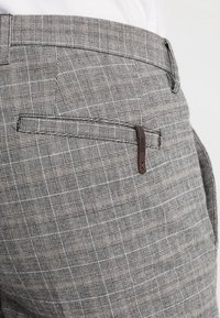 Šedé kostkované kalhoty s přizpůsobeným střihem, vyrobené z texturované tkaniny, s plochým předním dílem a jednou zadní kapsou s koženým detailem.