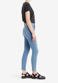 Jeans ajustados de color azul con un lavado claro y un ligero desgaste, combinados con una camiseta negra de manga corta y sandalias negras de suela gruesa.