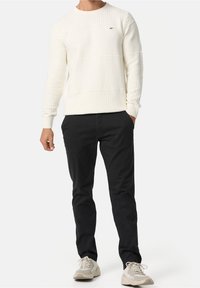 Witte gebreide trui met een textuur en horizontale strepen, gecombineerd met zwarte broek en lichte sneakers. Eenvoudig ontwerp en neutrale kleuren.
