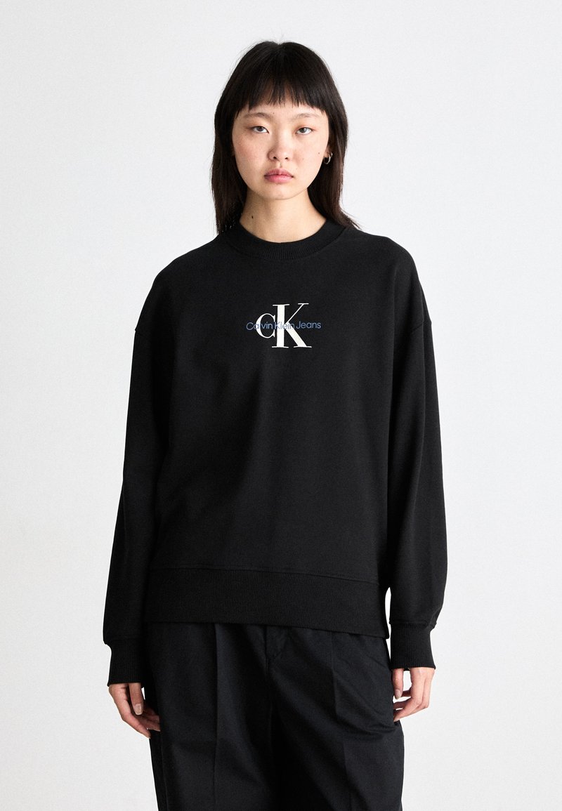 Črna bombažna majica s krožnim vratom in rebrastimi manšetami, ki na sprednji strani prikazuje belo in modro "CK Calvin Klein Jeans" logo.