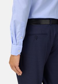 Světle modrá kostkovaná košile s manžetami na knoflíčky, spárovaná s tmavými proužkovanými kalhotami, které mají knoflíkovou zadní kapsu a elegantní černý opasek.