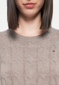 Bees värvitud kootud sviiter tekstuuriga kaablitootega, ümar kaelus ja rinnal väike logo, mis näitab punase, valge ja sinise värvi kombinatsiooni.