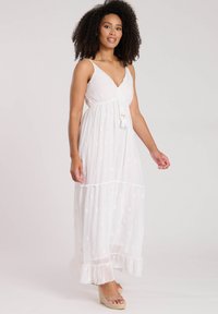 Witte maxi-jurk met een V-hals, dunne bandjes, tiered ruches aan de onderkant en gouden geborduurde bloemenpatronen. Zachte, lichte stof met een kwastaccent.