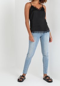 Svart satinramad topp med spetsdetaljer, ihopparad med ljusblå skinny jeans och svarta sandaler med dekorativa pärldetaljer.