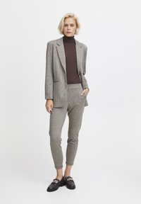 Takk blazer ja buksit beežis ja pruunis koos sobiva kõrge kaelusega särk. Riietusel on kohandatud disain ja õrn sära. Mustad loafers kuldsete aktsentidega.