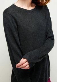 Tumma harmaa pitkähiha sweater, joka on valmistettu teksturoidusta kankaasta. Siinä on pyöreä pääntie ja istuvat hihat, joissa on pidennetyt kalvosimet.