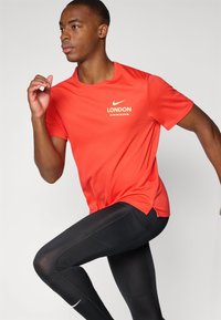 Κόκκινο αθλητικό μπλουζάκι κοντομάνικο με στρογγυλή λαιμόκοψη και άσπρη γραφική εκτύπωση "LONDON". Συνδυάζεται με μαύρες κολάν που διαθέτουν σχεδιασμό εφαρμοστό.