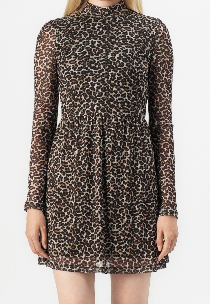 Femme portant une robe courte à manches longues et col montant, avec un motif léopard marron et noir.