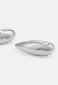 Dos objetos pulidos en forma de lágrima hechos de plata, con superficies lisas, un acabado reflectante y extremos redondeados.