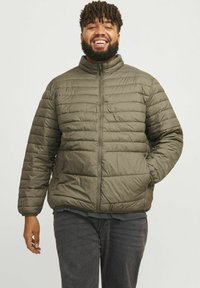 Olijfgroene pufferjack met horizontaal quiltpatroon, hoge kraag en rits aan de voorkant. Gemaakt in een relaxte pasvorm, van synthetisch materiaal.