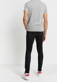 Camiseta gris de manga corta combinada con jeans pitillo negros y zapatillas blancas con detalles en rojo. Tejido suave y ajuste ceñido.