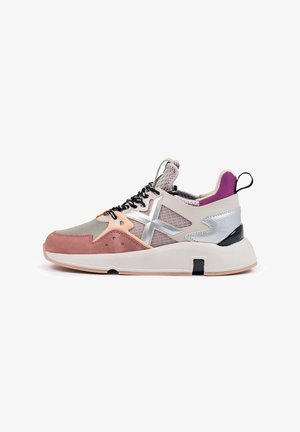 Zapatilla moderna con ante rosa, malla beige, detalles metálicos plateados, cordones negros y blancos, forro interior morado y suela blanca gruesa.
