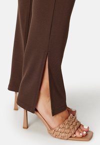 Brązowe, dopasowane spodnie z bocznymi rozcięciami u dołu, w połączeniu z beżowymi plecionymi sandałami na obcasie typu szpilka, z kwadratowym noskiem.