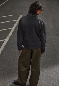 Jachetă din denim negru cu o croială relaxată, având un guler clasic și cusături vizibile. Asortată cu o pereche de pantaloni largi de culoare verde măslin.