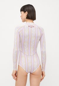 Long-sleeve wetsuit in pastel lavender with gold and white wavy patterns and logo detail on the back, made from stretchable material.