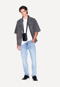 Camicia nera a maniche corte con fantasia, t-shirt bianca, jeans chiari strappati, e sneakers nere. Piccola borsa a tracolla nera.